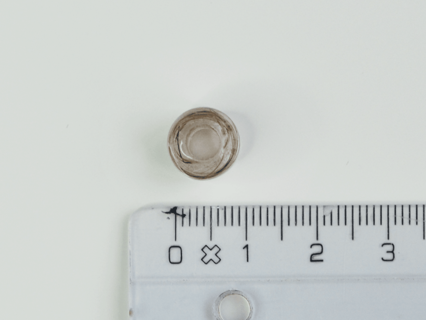 Thea perle – håndlavet resinperle med hundehår snøret rundt i perlen. Hul i midten (4 mm) – vist liggende med lineal