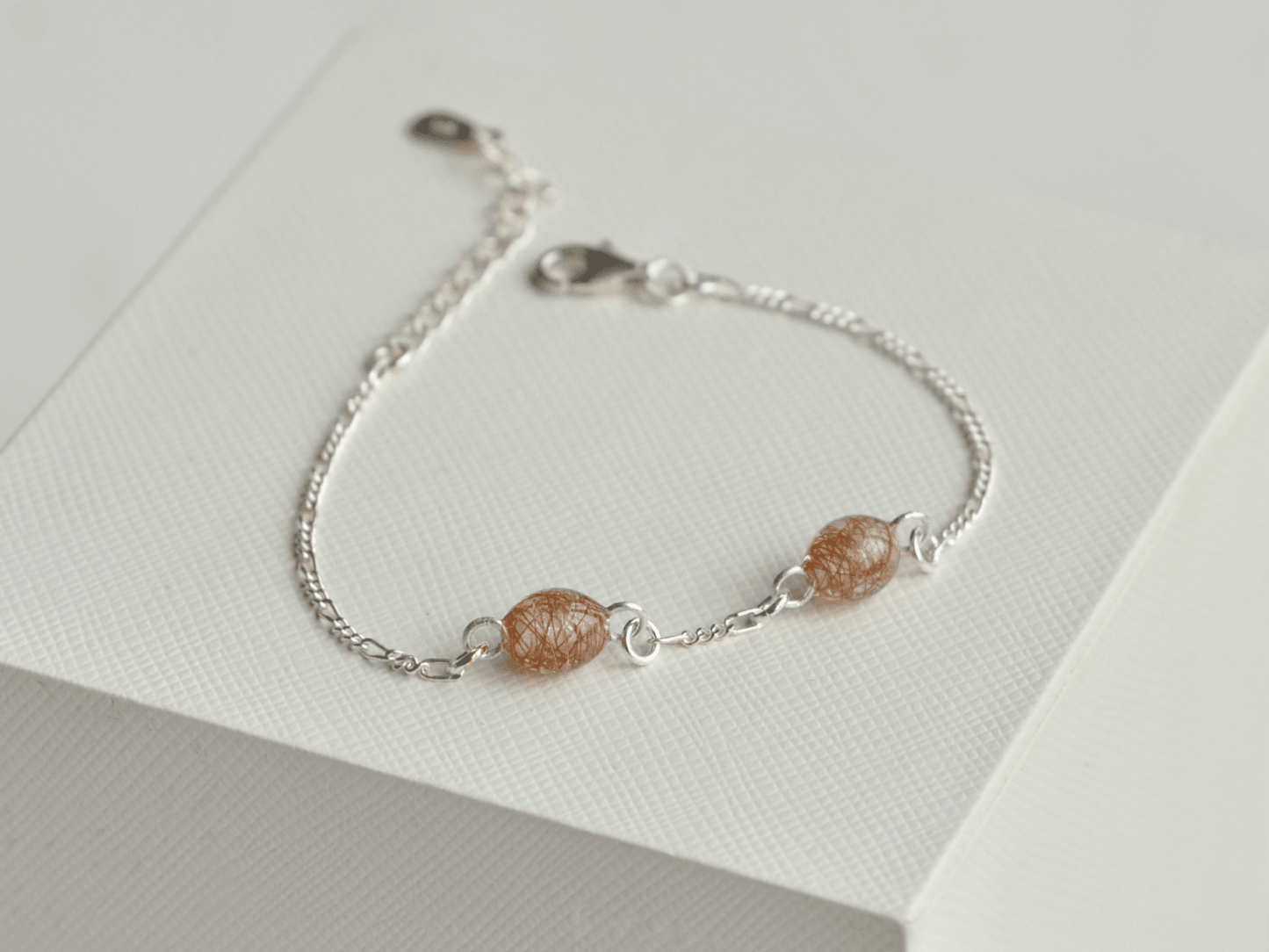 Lærke armbånd i 925 sterling sølv med to håndlavede resinperler i perlehvid med rødt hår fra to forskellige røde heste – set lidt fra siden