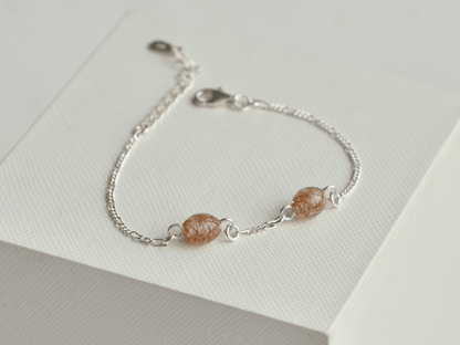 Lærke armbånd i 925 sterling sølv med to håndlavede resinperler i perlehvid med rødt hår fra to forskellige røde heste – set lidt fra siden