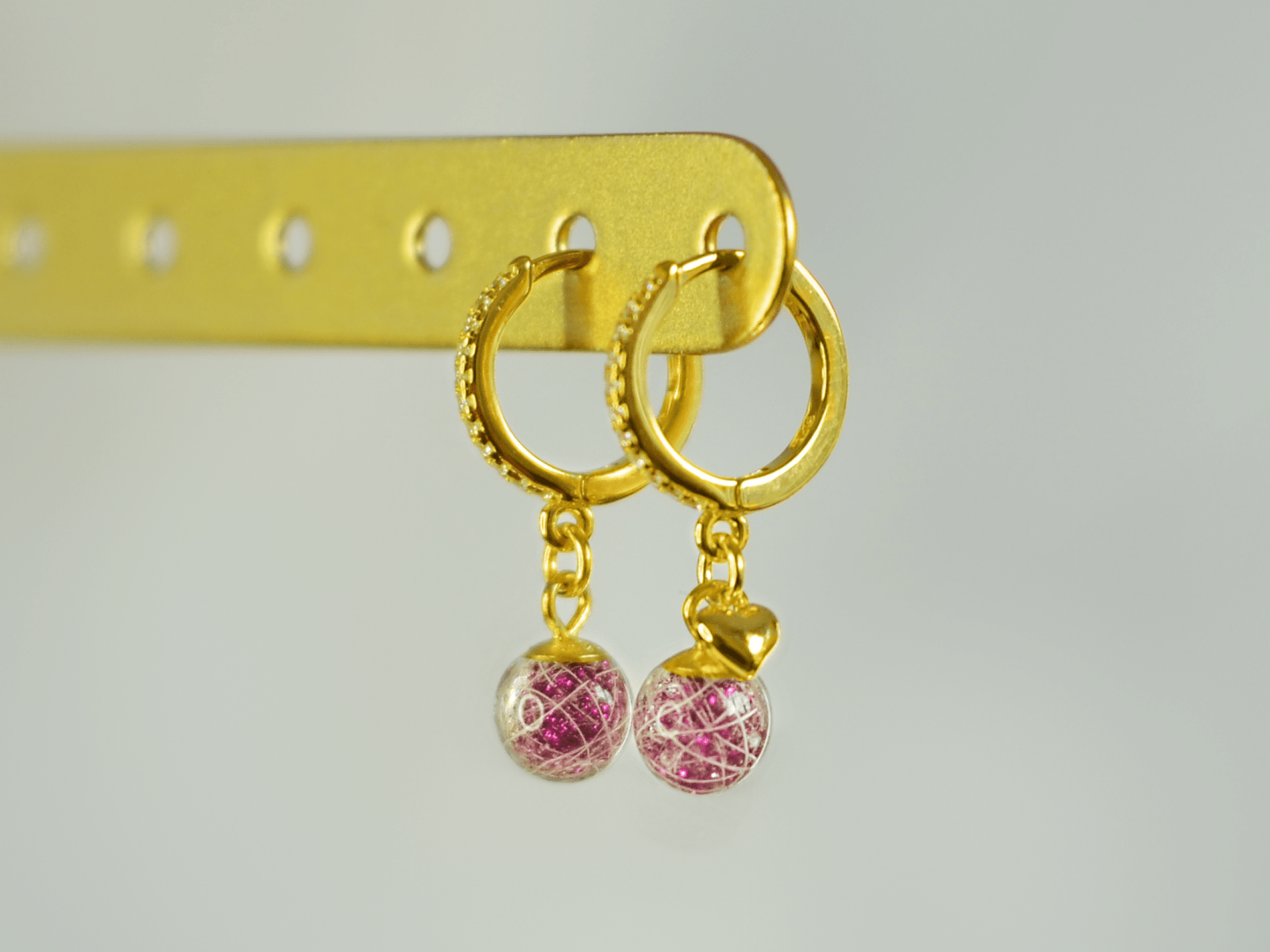 Lusia øreringe i forgyldt 925 sterling sølv med rhinestones og to håndlavede resinperler med hår fra palomino pony. Lyserødt glimmer i perlen fremhæver de hvide hår. Set fra siden med fokus på øreringen med minihjerte.