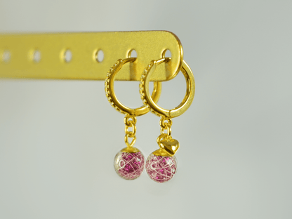 Lusia øreringe i forgyldt 925 sterling sølv med rhinestones og to håndlavede resinperler med hår fra palomino pony. Lyserødt glimmer i perlen fremhæver de hvide hår. Set fra siden med fokus på øreringen med minihjerte.