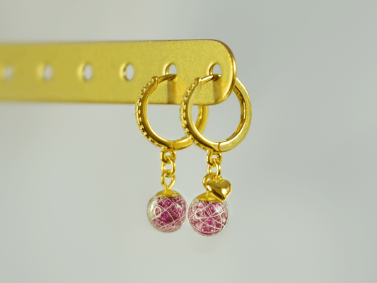 Lusia øreringe i forgyldt 925 sterling sølv med rhinestones og to håndlavede resinperler med hår fra palomino pony. Lyserødt glimmer i perlen fremhæver de hvide hår. Set fra siden med fokus på øreringen med minihjerte.